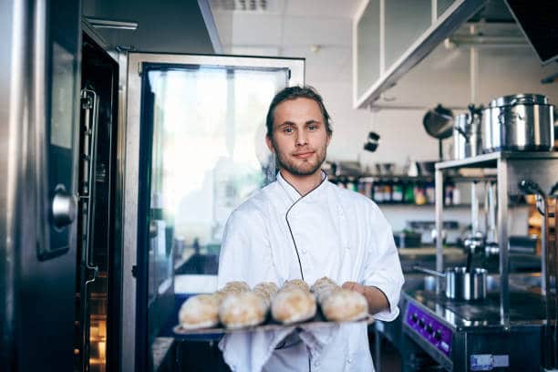 Jeune boulanger qui tient un plateau de petits pains