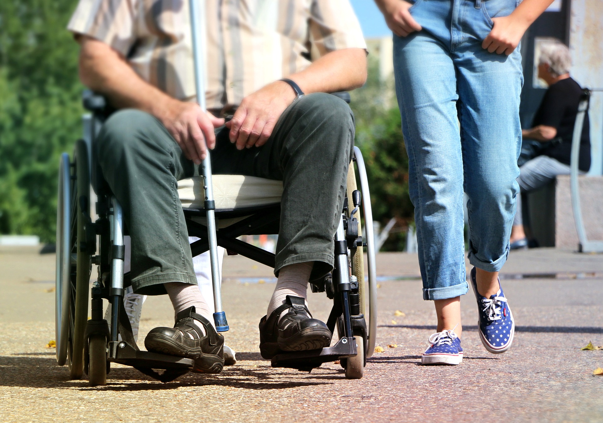 Homme en fauteuil roulant accompagné par une jeune personne qui marche à côté