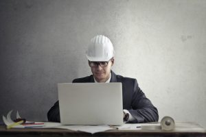 homme portant un casque de chantier devant son ordinateur